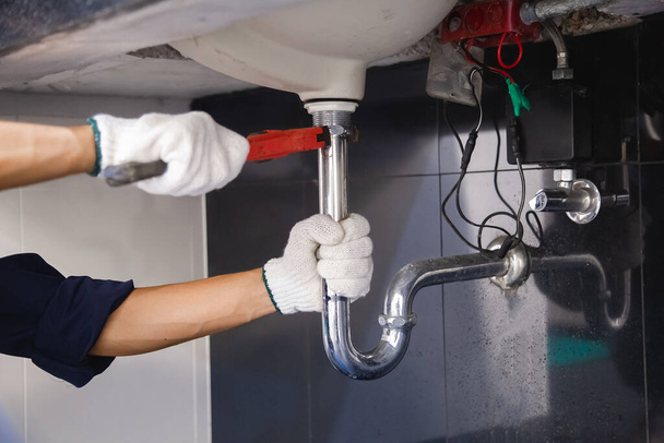 Plumber fixing white sink pipe with adjustable wrench. - Fotografie, Obrázek