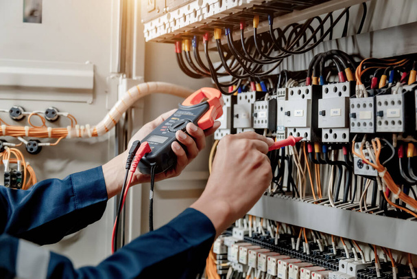 Elektricien ingenieur gebruikt een multimeter om de elektrische installatie en stroomleiding te testen in een schakelkast van een elektrisch systeem. - Foto, afbeelding