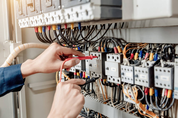 Inżynier elektryk wykorzystuje multimetr do testowania prądu instalacji elektrycznej i przewodu zasilającego w szafie sterowniczej układu elektrycznego. - Zdjęcie, obraz