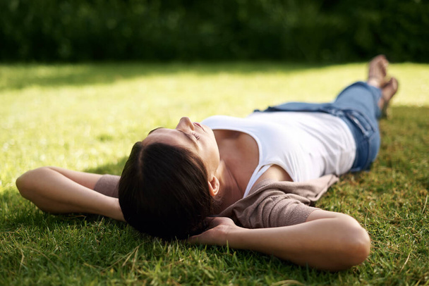 Taking the day off. High angle shot of a young woman lying on the grass. - Фото, изображение