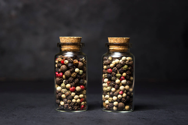 A mixture of peppercorns in a glass flask on a black background. Hot peppercorns. - Zdjęcie, obraz