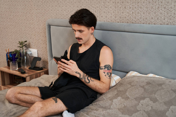 Carefree guy with mustache attentively messaging on mobile phone at home - Zdjęcie, obraz
