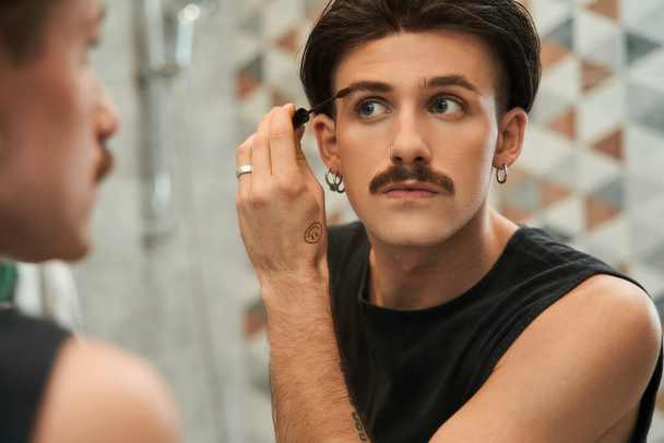 Handsome guy applying brow gel to his eyebrow while attentively looking at the mirror - Zdjęcie, obraz