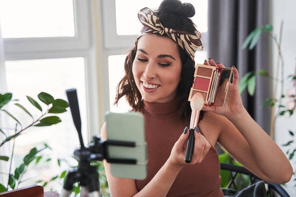 Young woman talking about cosmetics while holding makeup palette and brush - Foto, Imagem