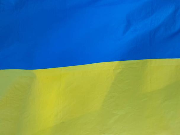 Блакитний і жовтий український прапор, що літає в небі при яскравому сонячному світлі. Зблизька текстиль прапора. Державний прапор України має дві рівнорозмірні горизонтальні смуги синього і жовтого кольорів. - Фото, зображення