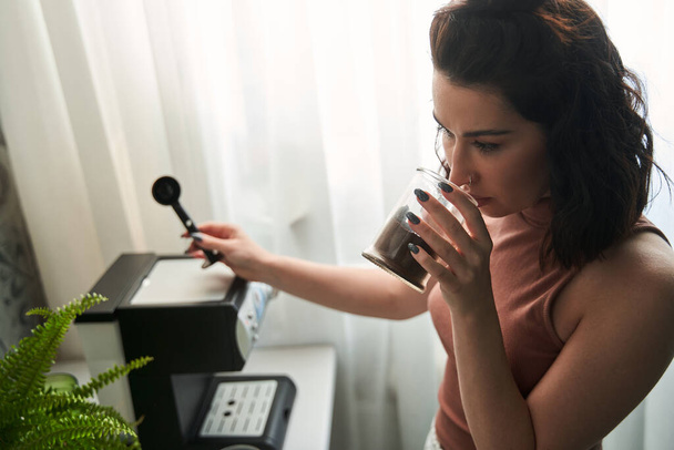 Brunette female holding jar with coffee and inhales aroma of it - 写真・画像