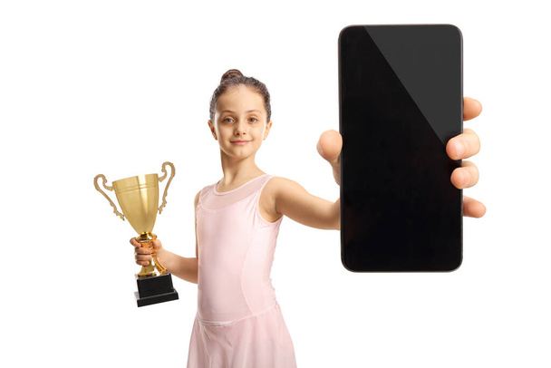 Ballerina in a pink dress holding a gold trophy cup and a smartphone isolated on white background - 写真・画像