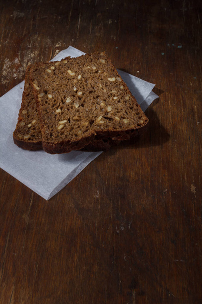 Two whole grain rye bread slices with seeds on parchment paper on wooden table. Copy space, vertical shot - Фото, зображення