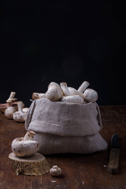 Natural fabric bag with fresh organic champignon mushrooms, autumn leaves, pine cones on rustic wooden background. Fall harvest, natural food. - Φωτογραφία, εικόνα