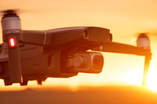 Bezzałogowy quadcopter w locie z cyfrową kamerą o zachodzie słońca. Sylwetka drona o zachodzie słońca - Zdjęcie, obraz