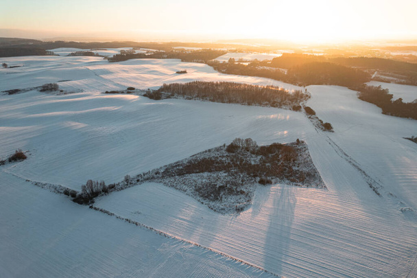 Aerial drone view of winter snow covered fields and forest at sunset - Fotoğraf, Görsel