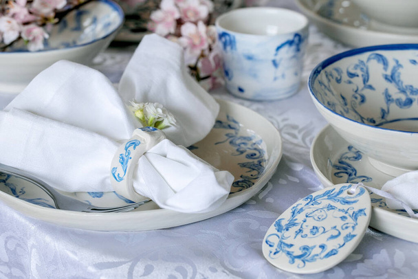 Elegant Easter table setting with empty marine ornament painted porcelain tableware, plates and bowls, Easter eggs decorations on white tablecloth. Easter holiday dinner. - Φωτογραφία, εικόνα