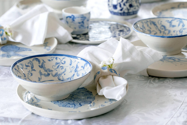 Elegant Easter table setting with empty marine ornament painted porcelain tableware, plates and bowls on white tablecloth. Easter holiday dinner. - Φωτογραφία, εικόνα