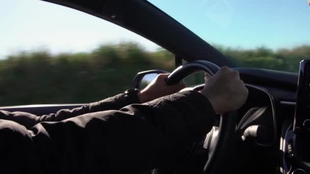 Close-up van de mannelijke handen houden stuurwiel in de moderne auto op road trip. Blanke man rijden nieuwe auto op de snelweg weg met mooie zonnige dag. - Video