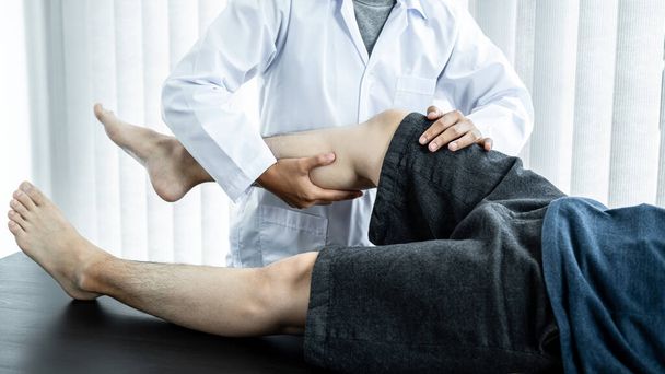Mężczyzna leżący na łóżku w celu uzyskania leczenia i rehabilitacji kontuzji kolana i nóg od fizjoterapeutki przez rozciąganie i ćwiczenia fizyczne z terapią w klinice zdrowia - Zdjęcie, obraz