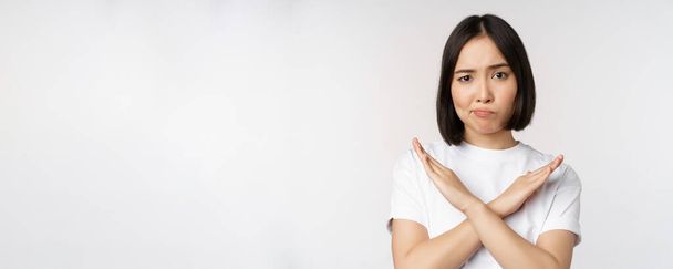 Portrait of asian korean woman showing stop, prohibition gesture, showing arm cross sign, standing in tshirt over white background - Photo, Image