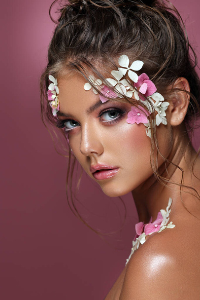 Beautiful caucasian woman with flowers on pink background. - Foto, afbeelding