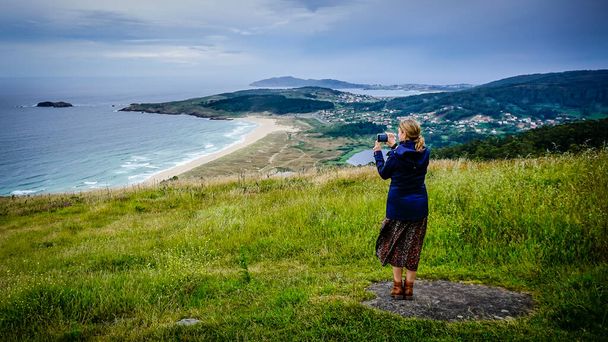 Young and beautiful woman taking photos with the mobile on the coast of Galicia - Fotó, kép