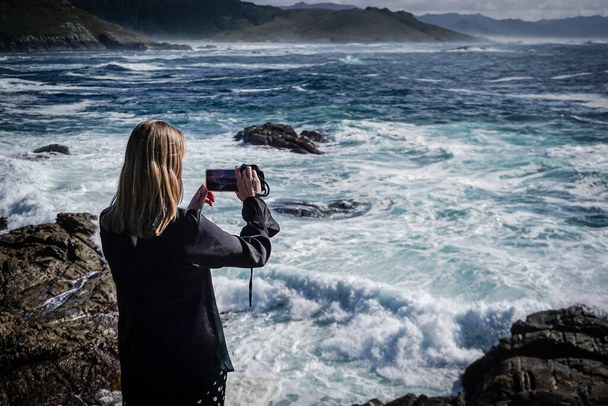 Junge und schöne Frau fotografiert mit dem Handy an der Küste von Galicien - Foto, Bild