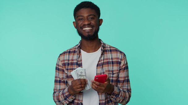 Happy african american man mobile phone display sincerely rejoicing win, receiving money dollar cash - Φωτογραφία, εικόνα