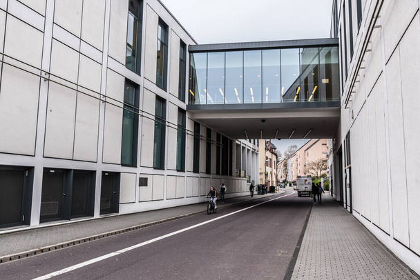 Трир, Рейнланд-Пфальц - Германия - 04 15 2019 - Девушка на велосипеде через заднюю улицу современного здания из стекла и стали - Фото, изображение