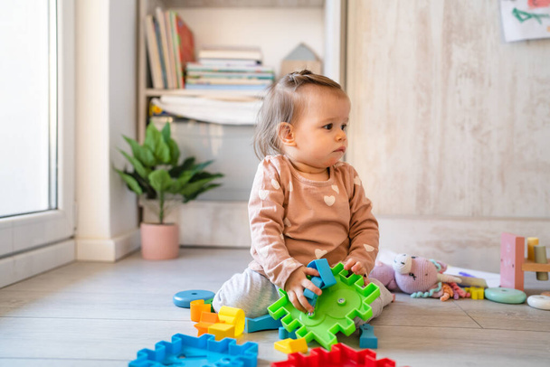 Um bebê pequena menina branca brincando no chão no espaço de cópia em casa segurando brinquedos de plástico na visão frontal do dia - Foto, Imagem