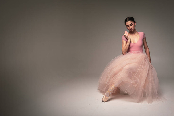 молодая красивая, хрупкая, красивая балерина танцует в длинном бледно-розовом платье с тюлем на однородном фоне, движениями рук, сдержанным тоном. Балет, танец, танцор. Место для надписи - Фото, изображение