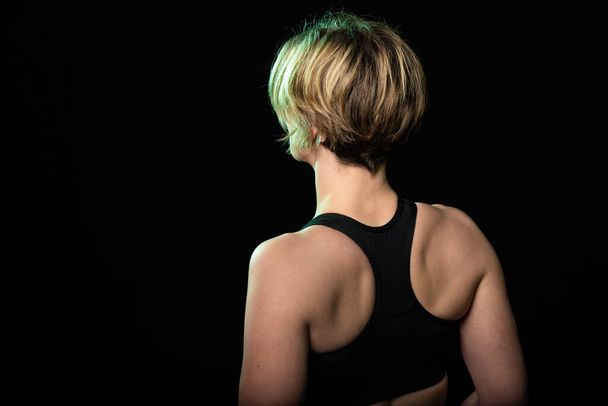 Low key studio portrait of a 35 year old white woman showing her back in a fitness top, Brussels - Foto, imagen