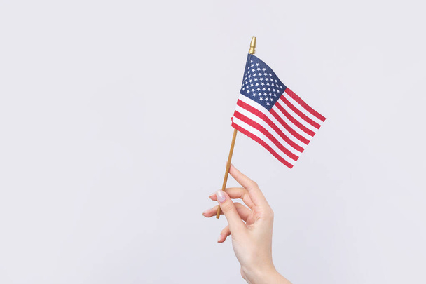 Una hermosa mano femenina sostiene una bandera americana sobre un fondo blanco. - Foto, imagen