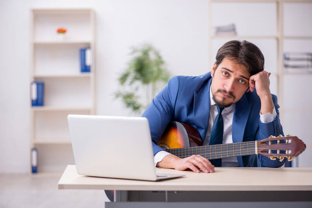 Jeune employé masculin jouant de la guitare sur le lieu de travail - Photo, image