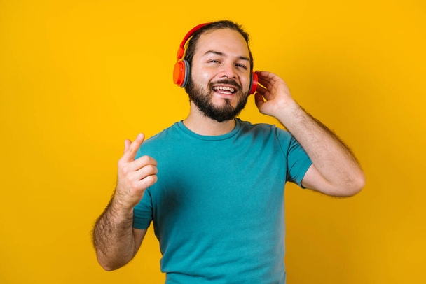 portrait of hispanic young man with headphones, dancing and listening music on yellow background in Mexico Latin America - Photo, Image