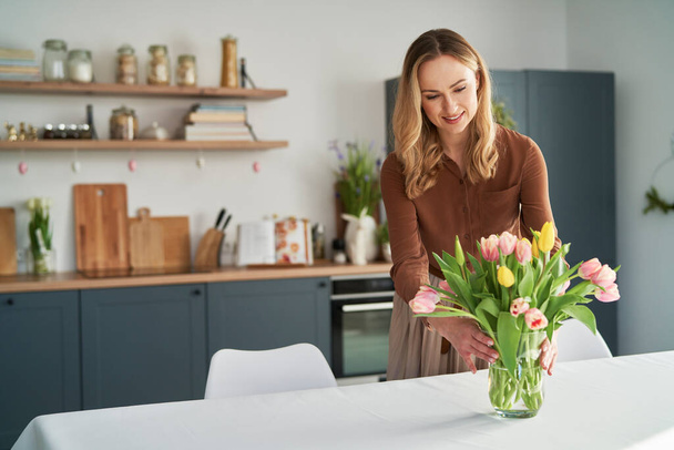 Caucasian woman putting fresh tulips into the vase - Foto, afbeelding