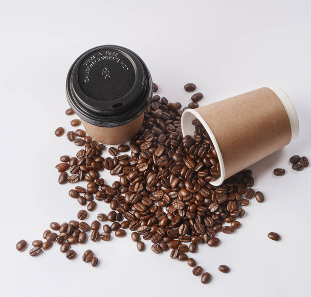 Start with Coffee. Studio shot of a tipped over paper cup filled with coffee beans against a grey background. - Valokuva, kuva