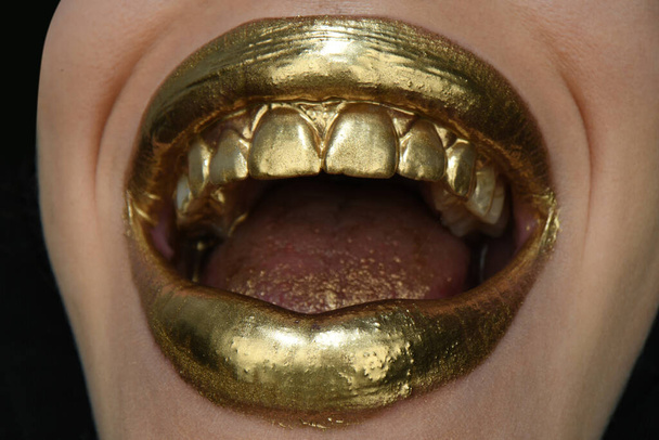 Gold lips. Gold paint from the mouth. Golden lips on woman mouth with make-up. - Photo, image
