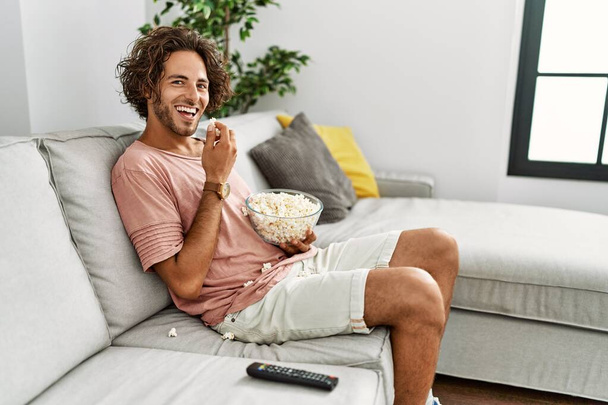 Joven hispano viendo una película sentada en el sofá de su casa. - Foto, imagen