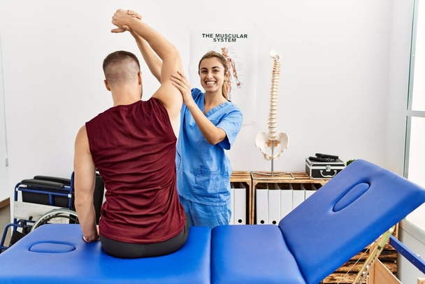 Young hispanic physioterapist woman make arm rehab treatment to man at the clinic. - Photo, Image