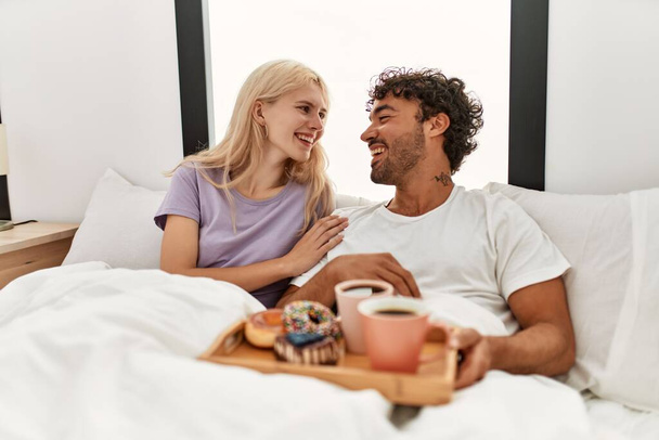 Jeune beau couple souriant heureux de prendre le petit déjeuner sur le lit à la maison. - Photo, image