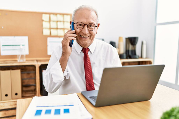 Ανώτερος εργαζόμενος επιχειρηματίας μιλάει στο smartphone που εργάζεται στο γραφείο - Φωτογραφία, εικόνα