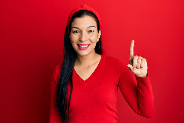 Jeune femme latine portant des vêtements décontractés souriant avec une idée ou une question pointant du doigt avec un visage heureux, numéro un  - Photo, image