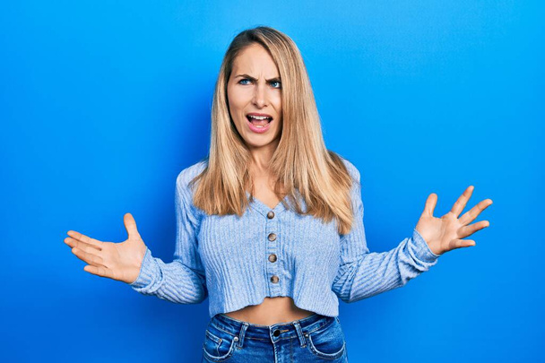 Young caucasian woman wearing casual clothes crazy and mad shouting and yelling with aggressive expression and arms raised. frustration concept.  - Foto, Imagen
