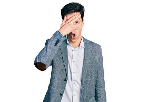 Young hispanic man wearing business clothes peeking in shock covering face and eyes with hand, looking through fingers with embarrassed expression.  - Photo, Image