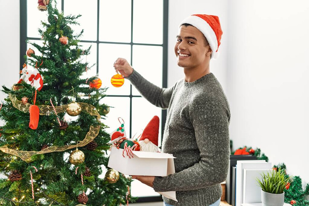 Fiatal spanyol férfi mosolygós magabiztos díszítő karácsonyfa otthon - Fotó, kép
