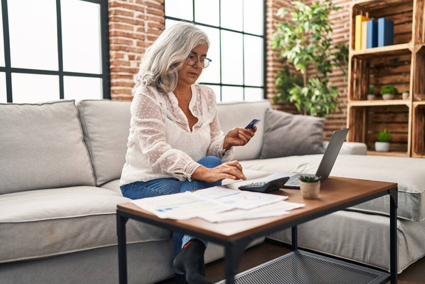 Женщина средних лет использует ноутбук и кредитную карту дома - Фото, изображение
