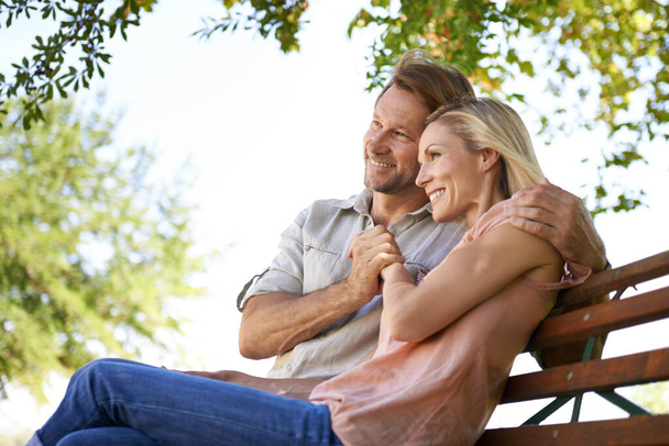 Love is inspired by the simplicity of nature. Shot of a happy mature couple sitting on a bench in the park. - Фото, изображение