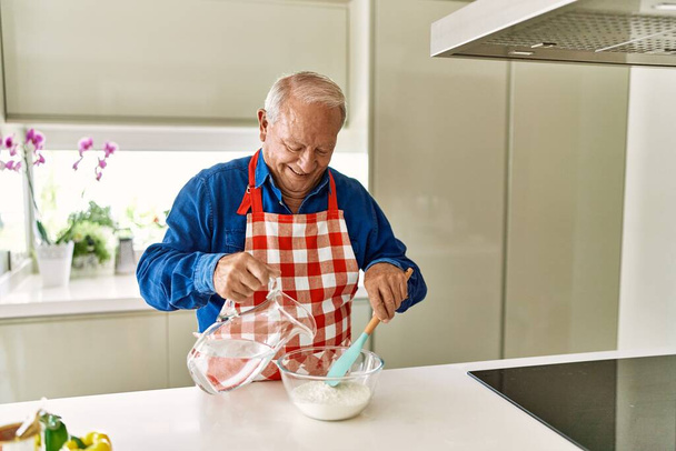 Senior man smiling confident cooking dough at kitchen - Photo, Image