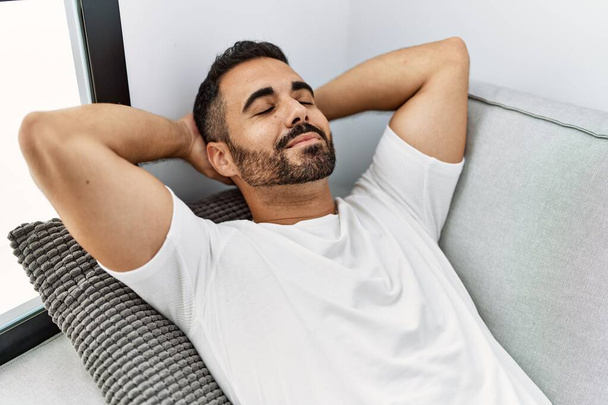 Young hispanic man relaxed with hands on head lying on sofa at home - Photo, Image