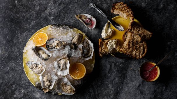 Oysters on ice with lemon, sauce, tartin bread and butter, sparkling wine. Marble background. Top view, horizontal - Photo, Image