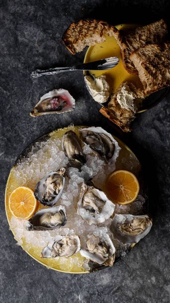Oysters on ice with lemon, sauce, tartin bread and butter, sparkling wine. Marble background. Top view, vertical - Photo, Image