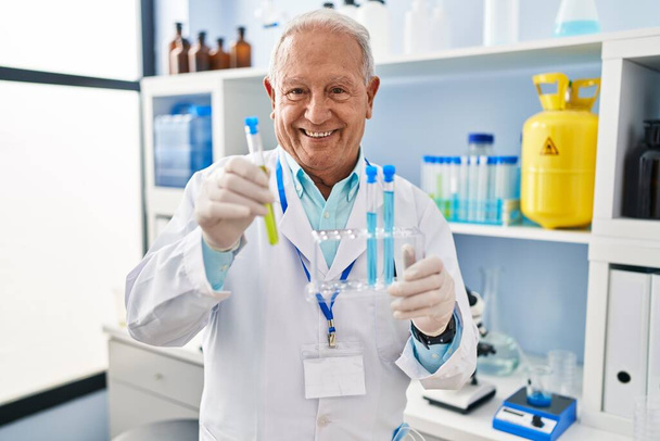 Idősebb férfi, aki tudományos egyenruhát visel, kémcsöveket tart a laborban. - Fotó, kép