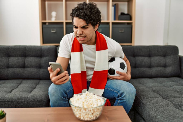 Young hispanic man watching soccer match and supporting team at home. - Zdjęcie, obraz